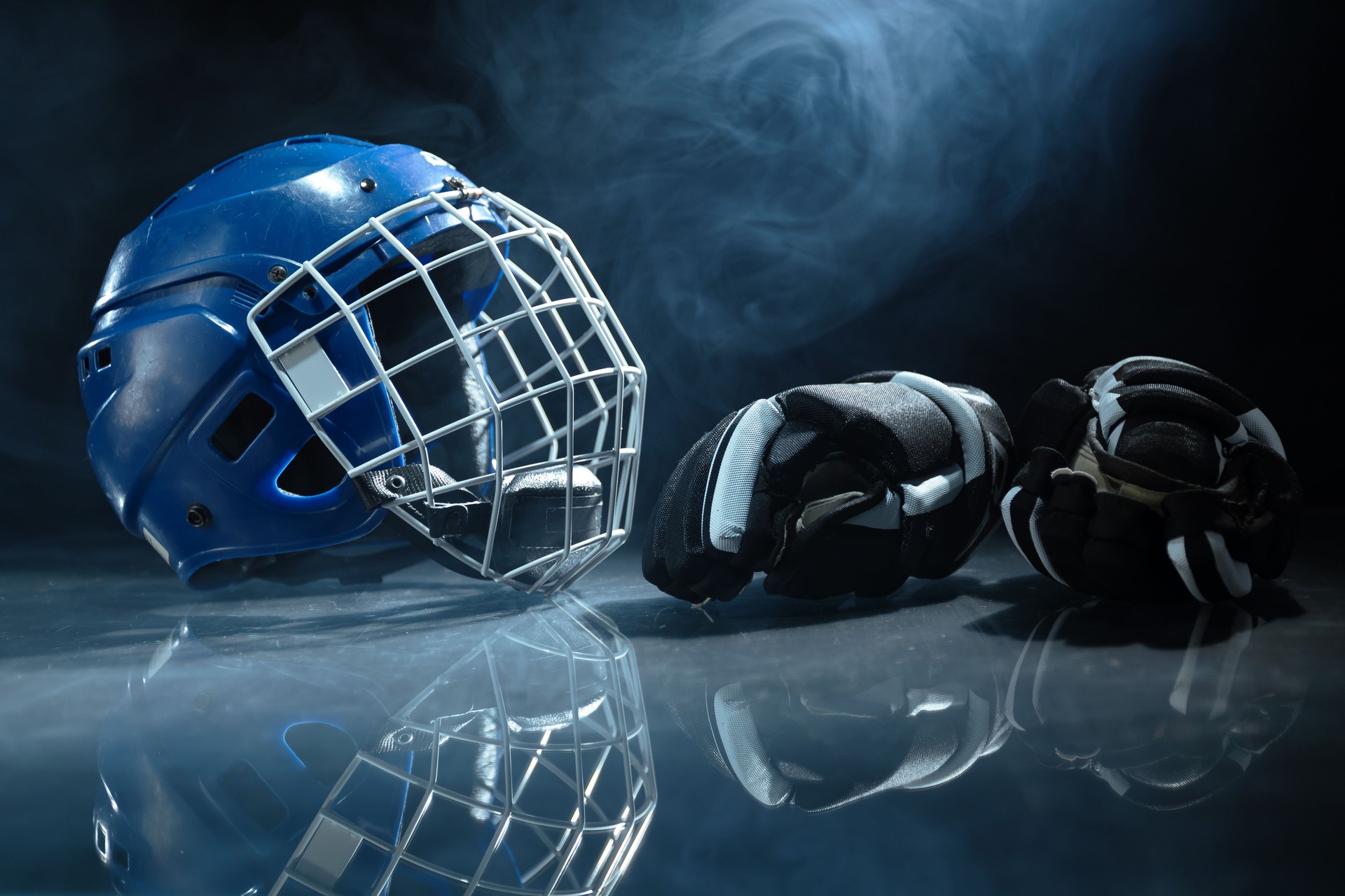 Close up on hockey helmet and hockey gloves lying down on reflecting surface.